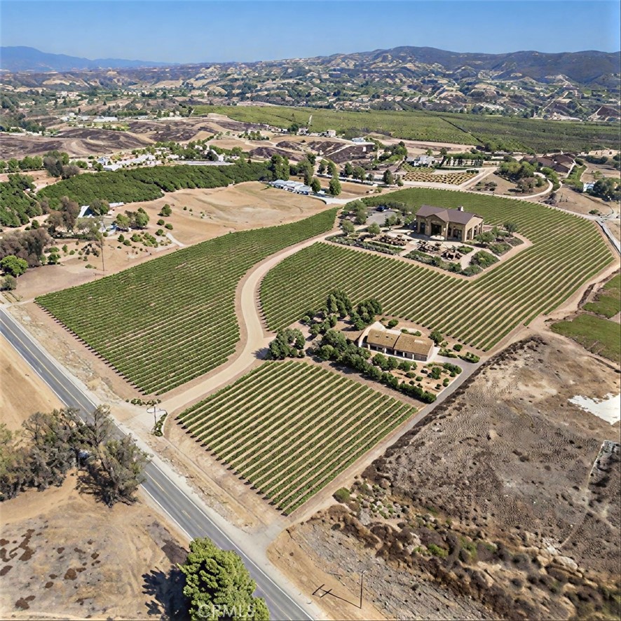 Aerial view of a vineyard estate with curved vine rows and buildings among dry hills.