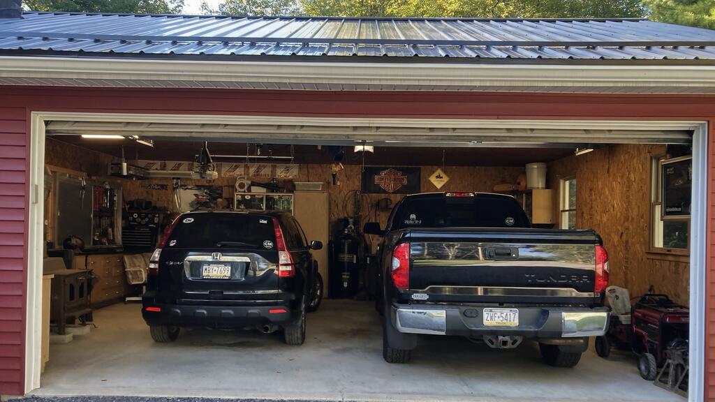 Two-car garage with a black SUV and pickup truck parked inside, plus workbenches and tools.