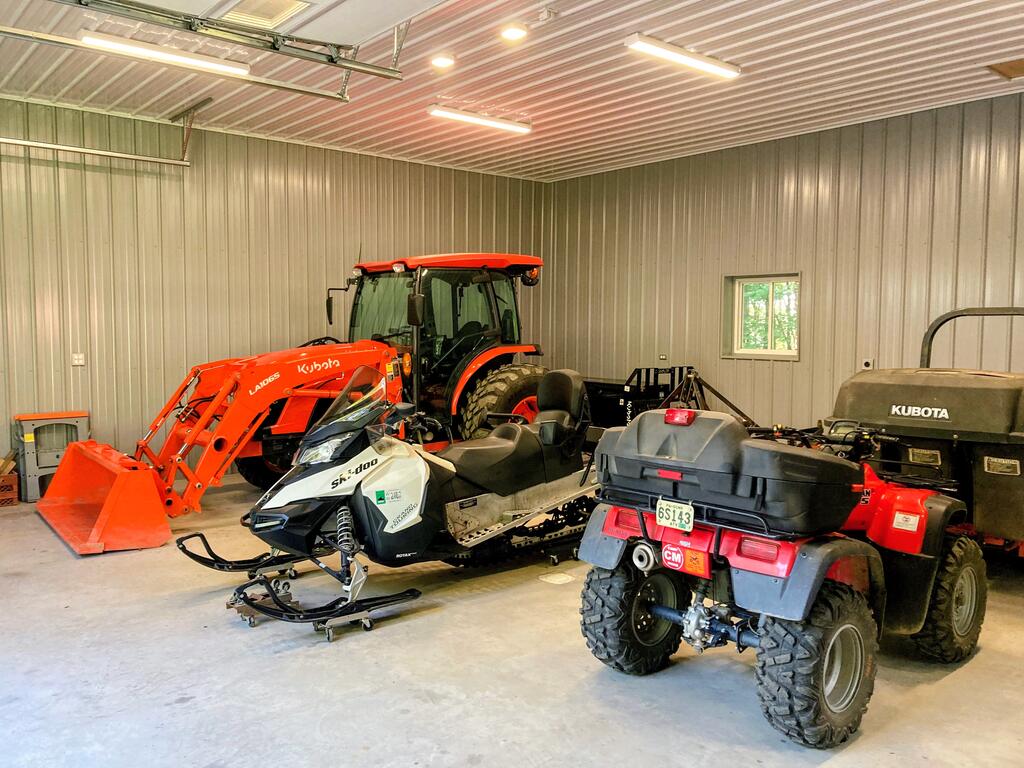 Large metal-walled garage housing an orange tractor, a snowmobile, and two ATVs.