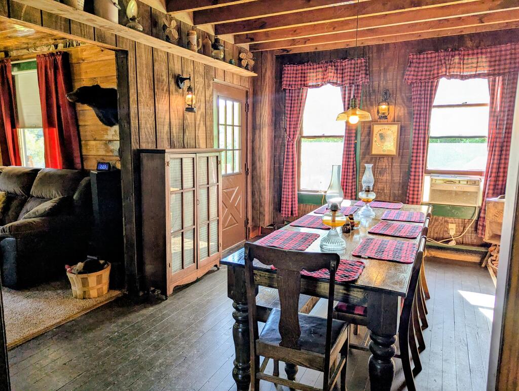 Rustic dining room with a wooden table, plaid cushions, exposed beams, and an adjoining living area.