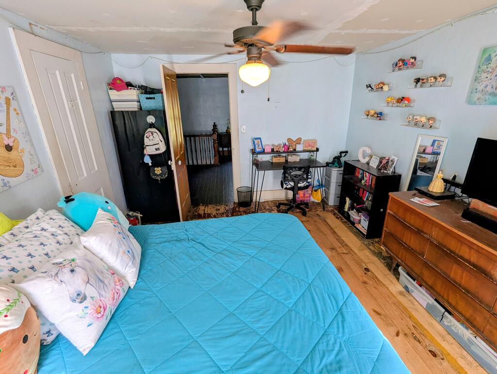 Bedroom with a bright blue quilt, floral pillows, hardwood floors, and a ceiling fan.