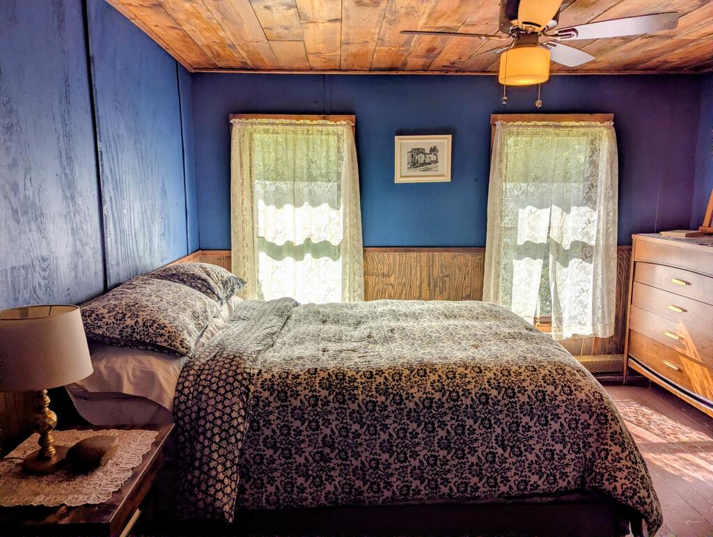 Bedroom with a floral-patterned bedspread, blue walls, and a wood-plank ceiling.