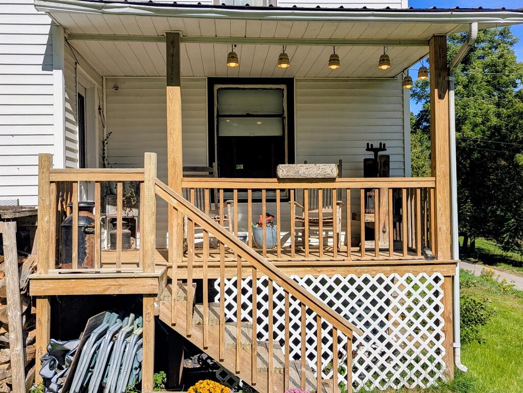 House with a covered wooden porch, hanging lights, and stairs leading to the yard.