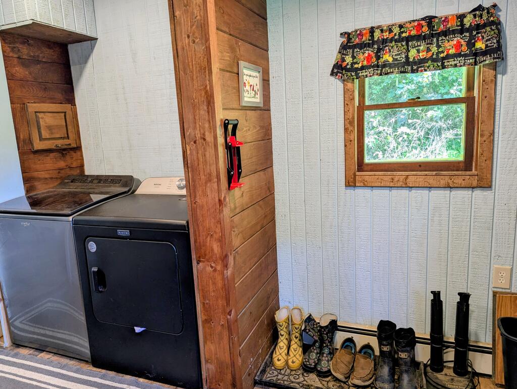 Laundry and mudroom with washer and dryer, rustic wood partition, and boots lined beneath a window.