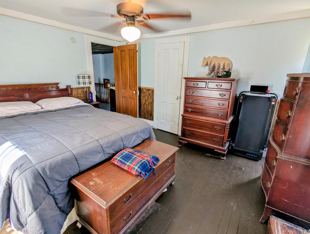 Furnished bedroom with a large bed, wooden dressers, and a ceiling fan.
