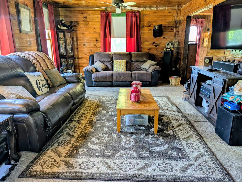 Rustic log-walled living room with leather sofas, a patterned rug, and a wooden coffee table.