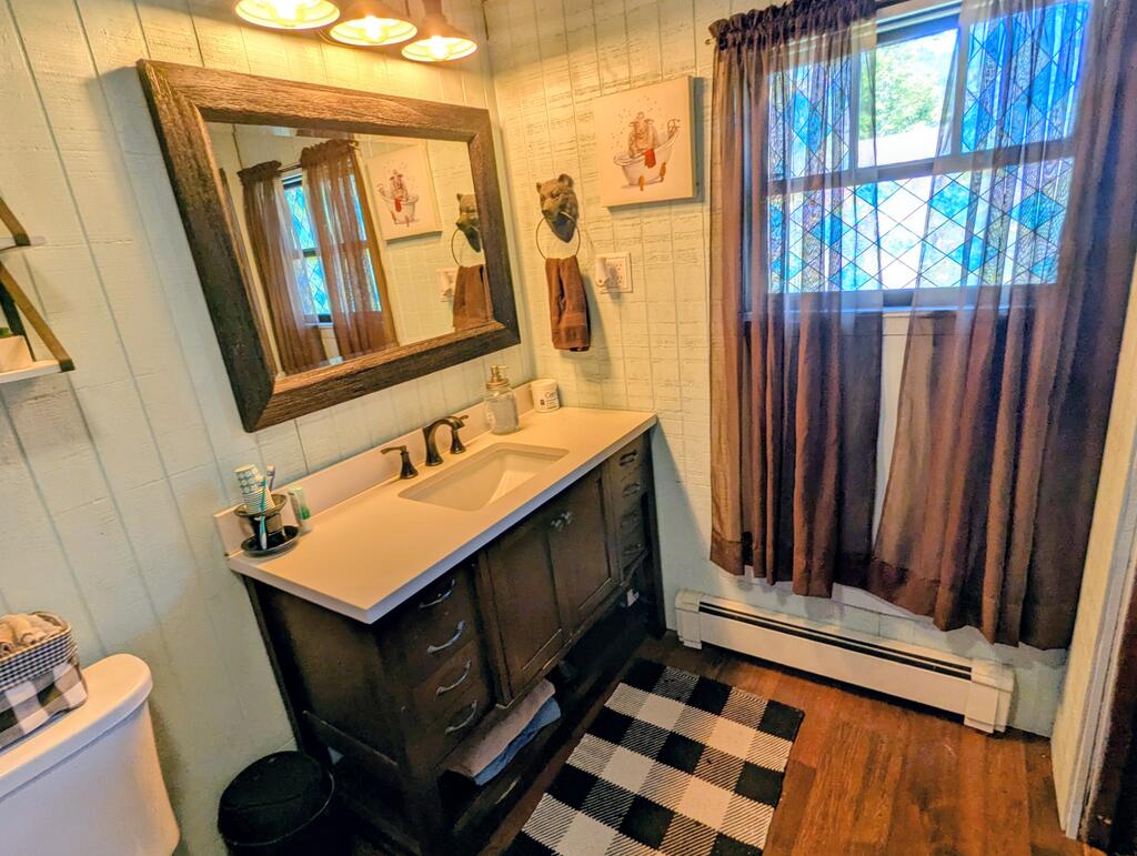 Bathroom with a dark wood vanity and large mirror beside a curtained, diamond-paned window.