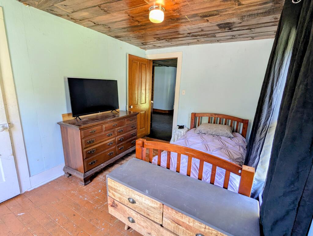 Bedroom with a wooden bed, television on a dresser, and weathered plank ceiling.