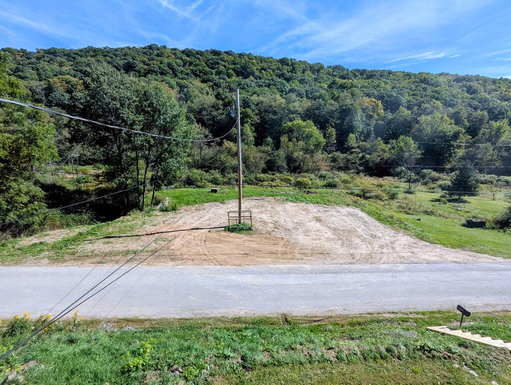 Cleared roadside lot with a utility pole, grassy edges, and wooded hills beyond.