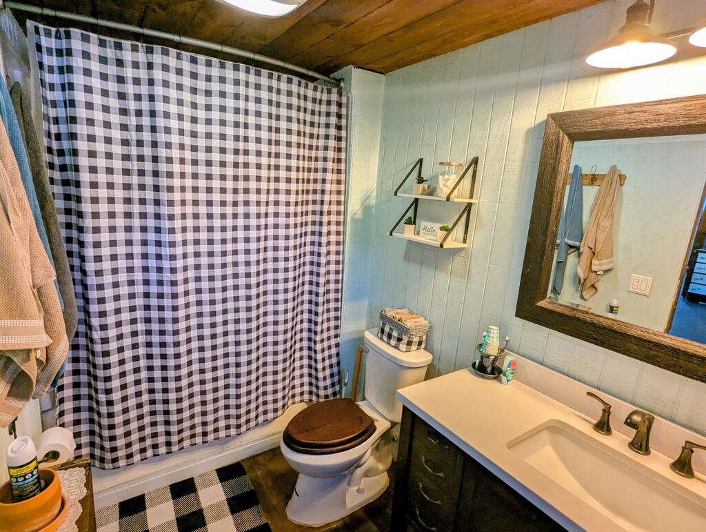 Bathroom with checkered shower curtain, toilet, and white vanity beneath a wood-framed mirror.