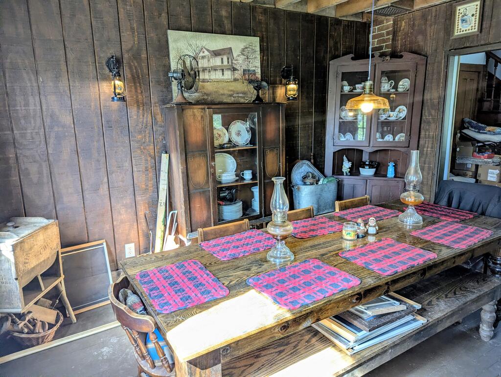 Rustic dining room with a long wooden table, plaid placemats, and antique china cabinets.