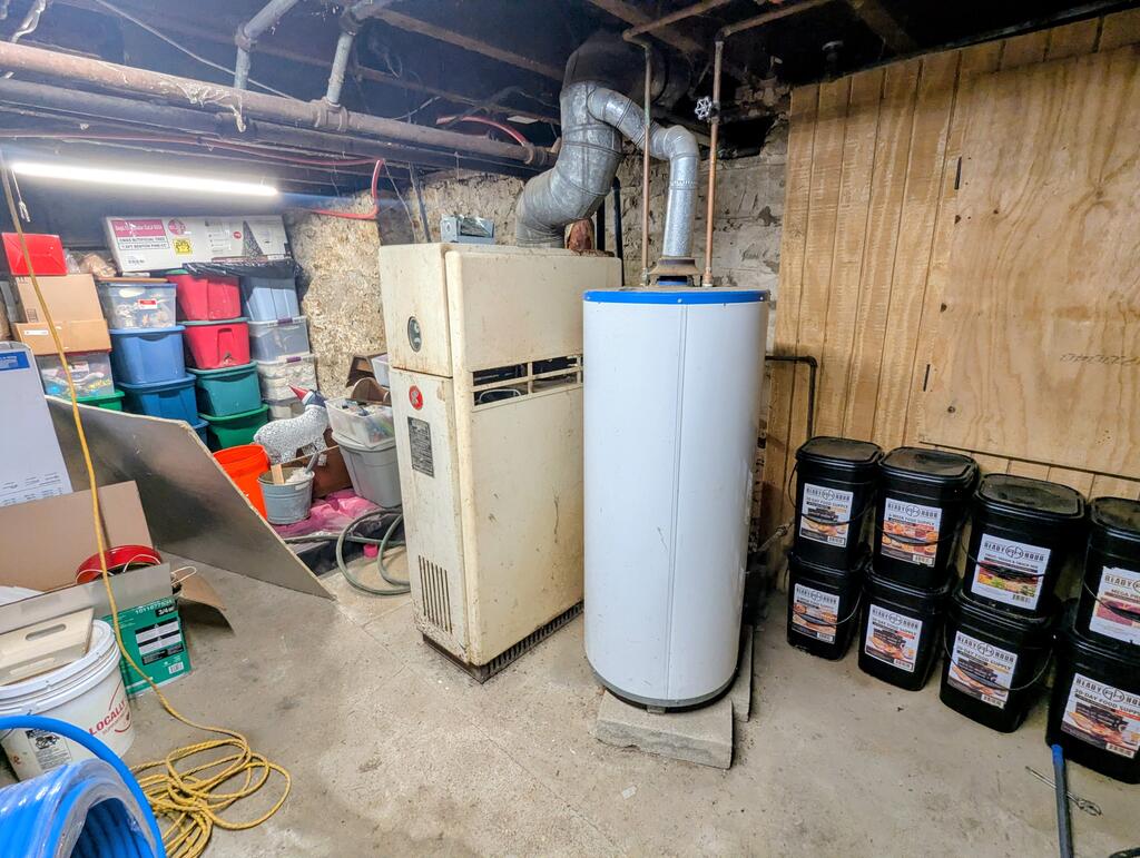 Basement utility room with a furnace, water heater, exposed ductwork, and stored supplies.