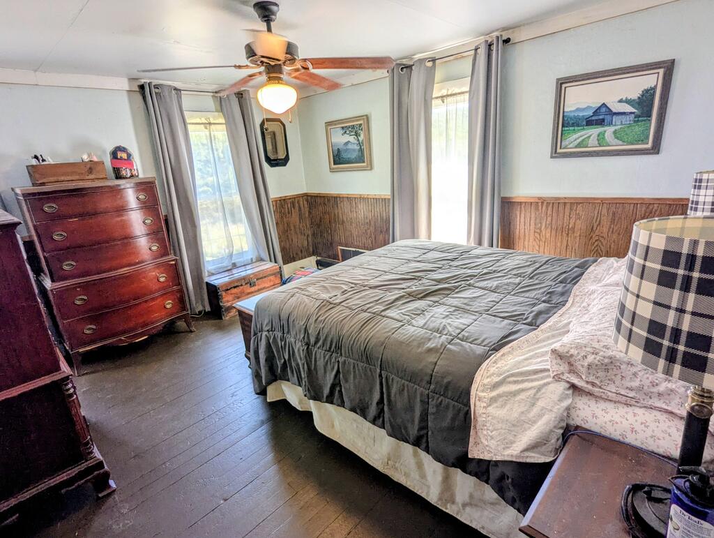 Furnished bedroom with a gray-quilted bed, wood-paneled walls, and tall curtained windows.