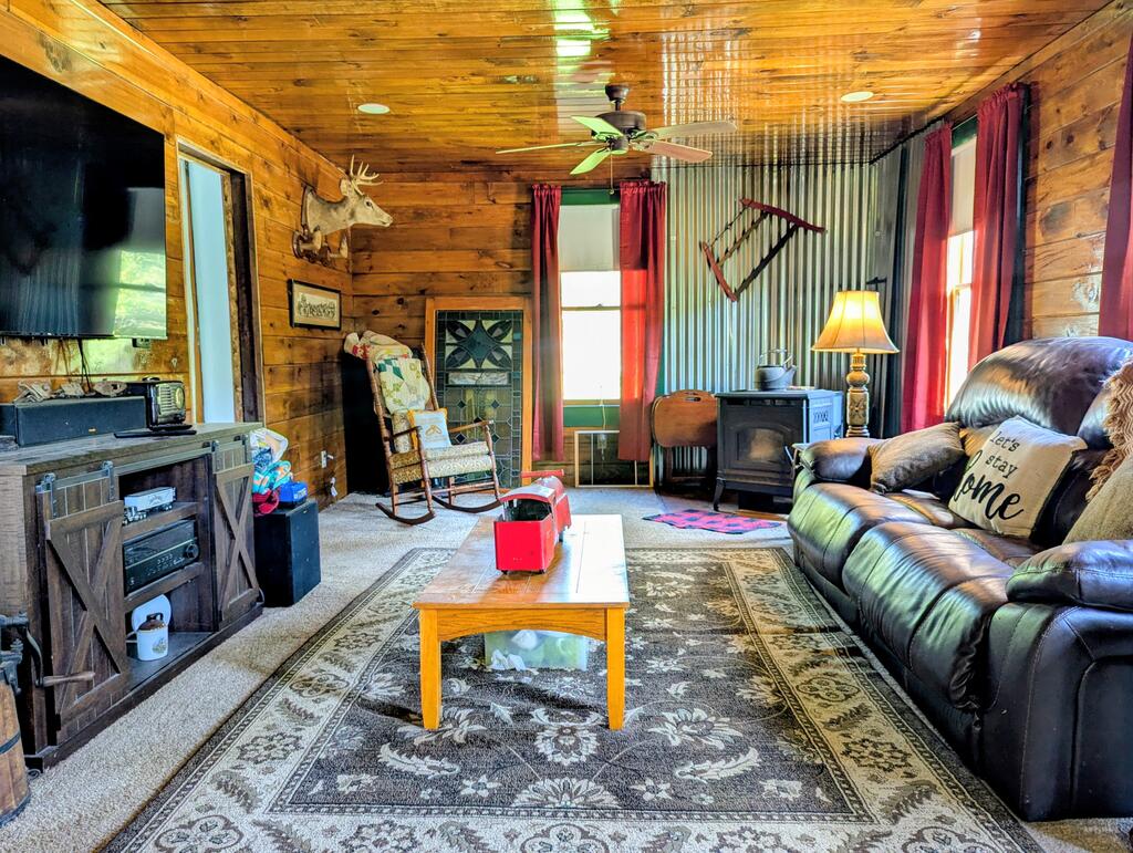 Wood-paneled living room with a leather sofa, rocking chair, and wood stove.