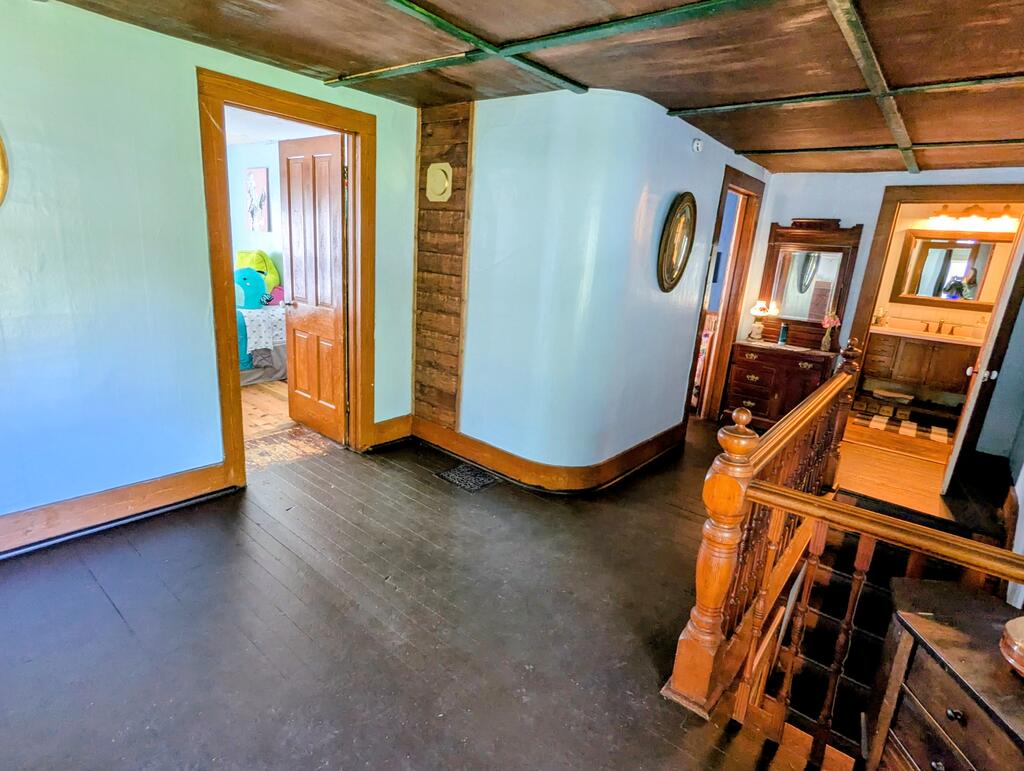 Upstairs hallway with a rustic wood ceiling, dark floors, and carved wooden stair railing.