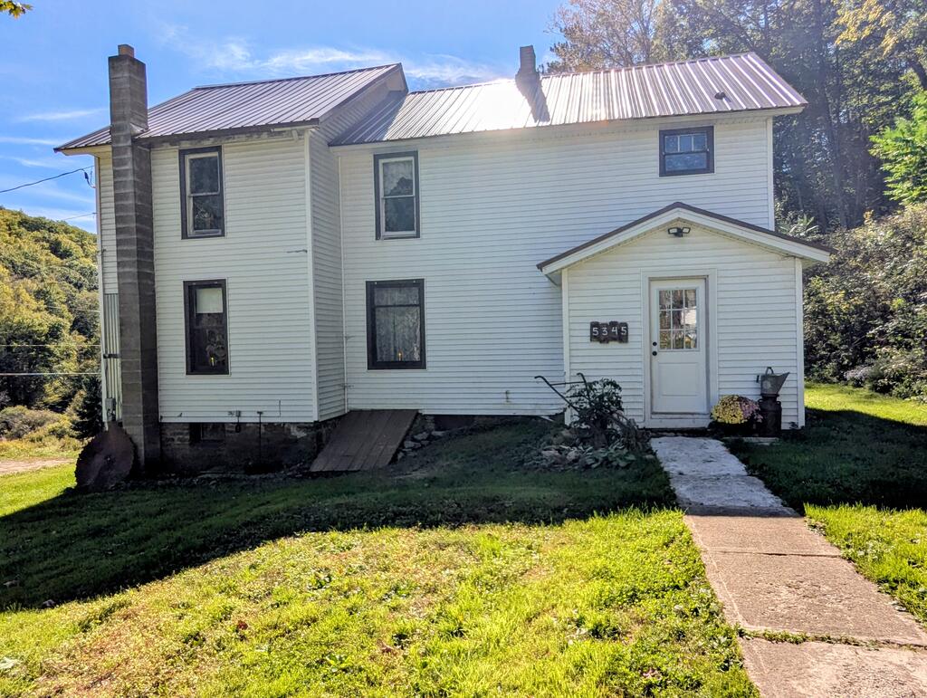 White two-story house with a metal roof, tall brick chimney, and walkway leading to the front door.