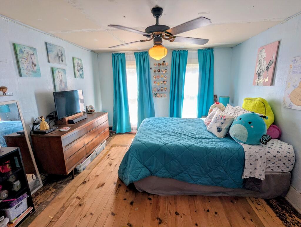 Bedroom with teal bedding, turquoise curtains, hardwood floors, and a ceiling fan.