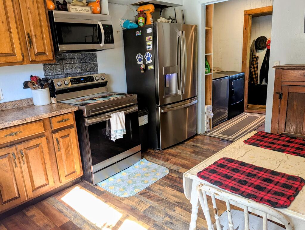 Kitchen with wood cabinets, stainless steel appliances, and a table with plaid cushions.