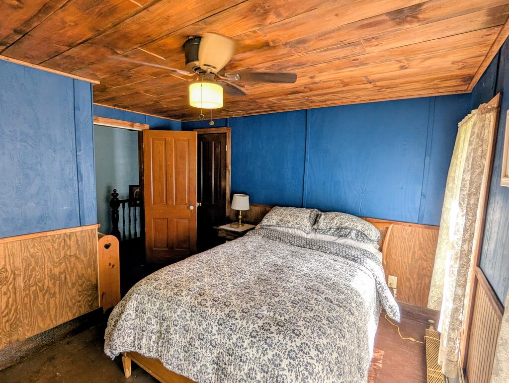 Bedroom with a patterned bedspread, deep blue walls, and a wood plank ceiling.