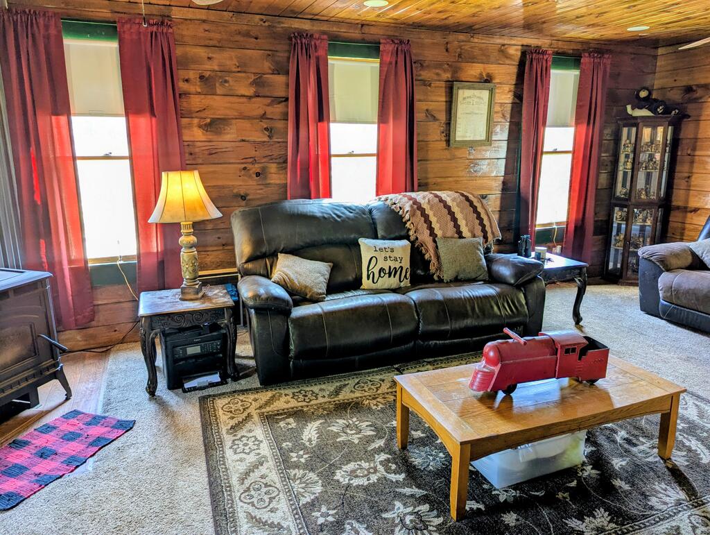 Rustic wood-paneled living room with a leather sofa, burgundy curtains, and a red model truck on the coffee table.