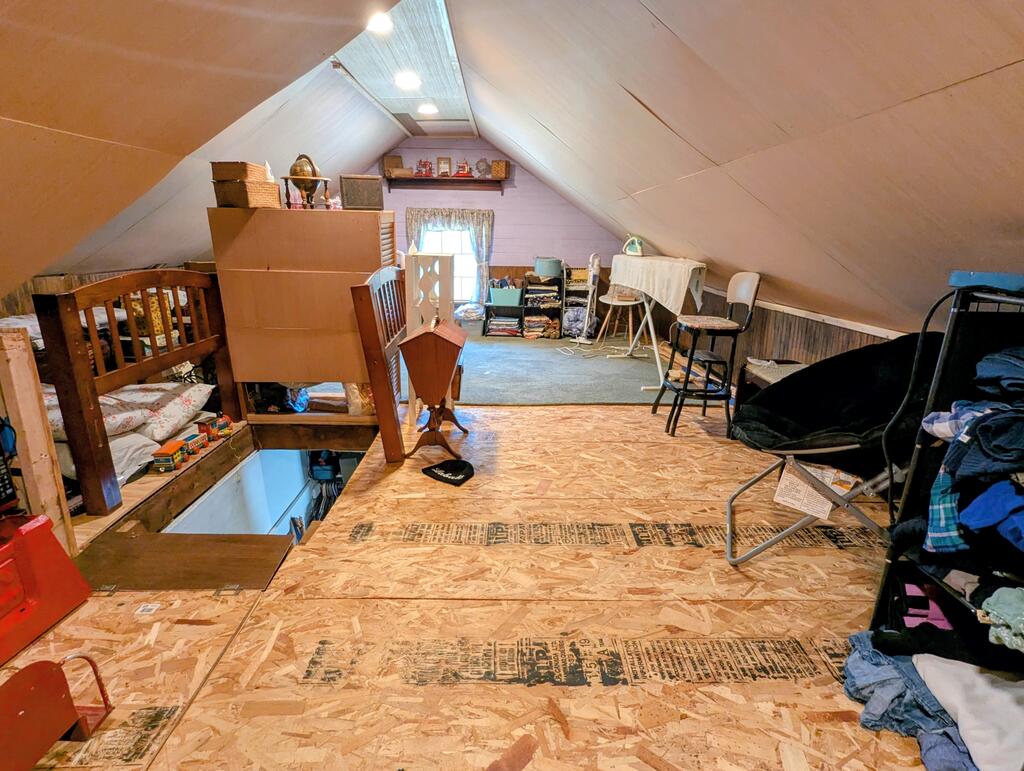 Attic loft with sloped ceilings, a small window, storage furniture, and an open floor hatch.