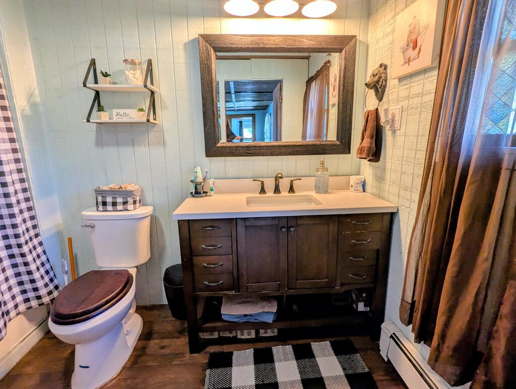 Bathroom with a dark wood vanity, framed mirror, and black-and-white checkered rug.