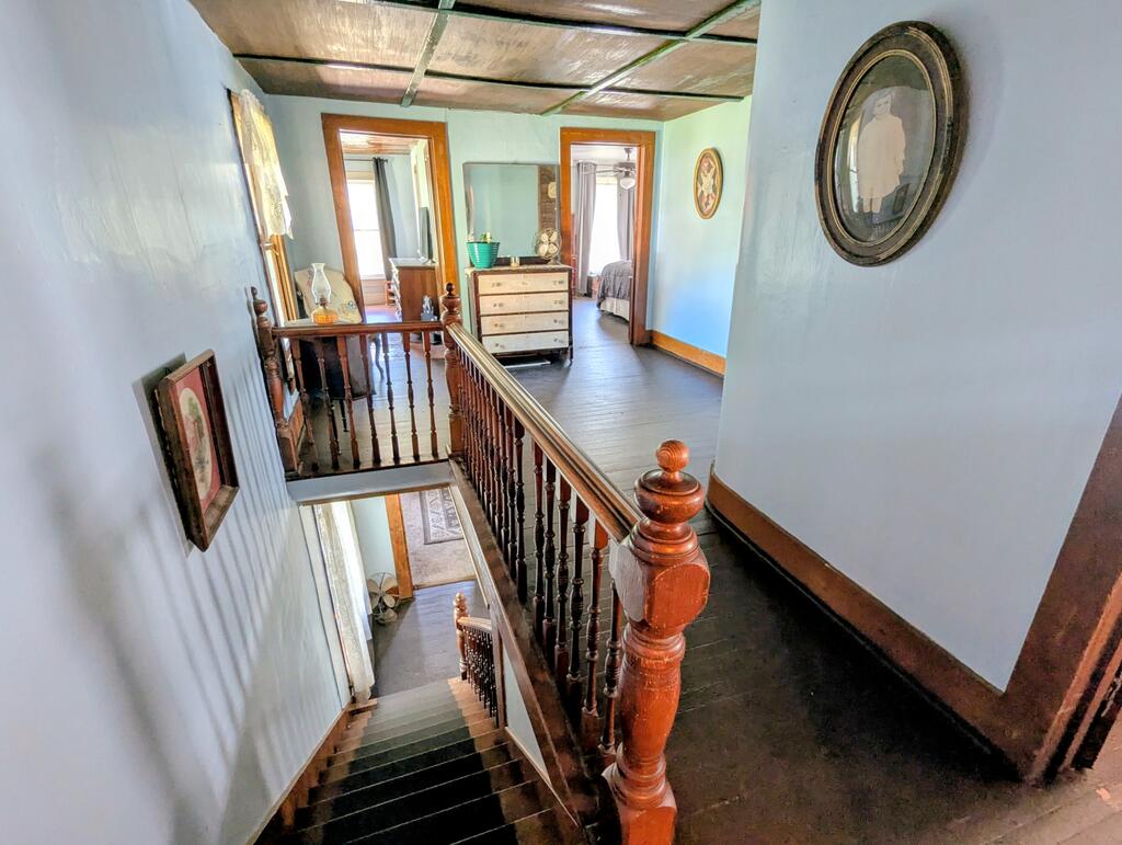 Upstairs landing with dark wood staircase, turned banisters, and a dresser between two bedroom doorways.