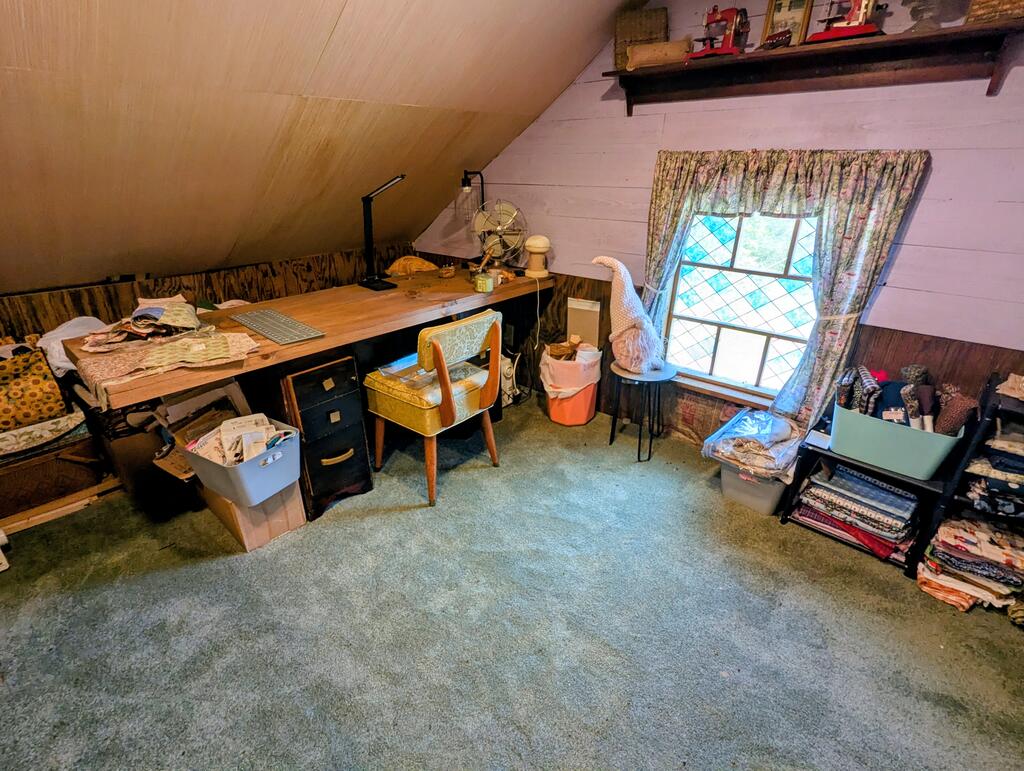 Home office with a long desk beneath a sloped ceiling and a curtained window.