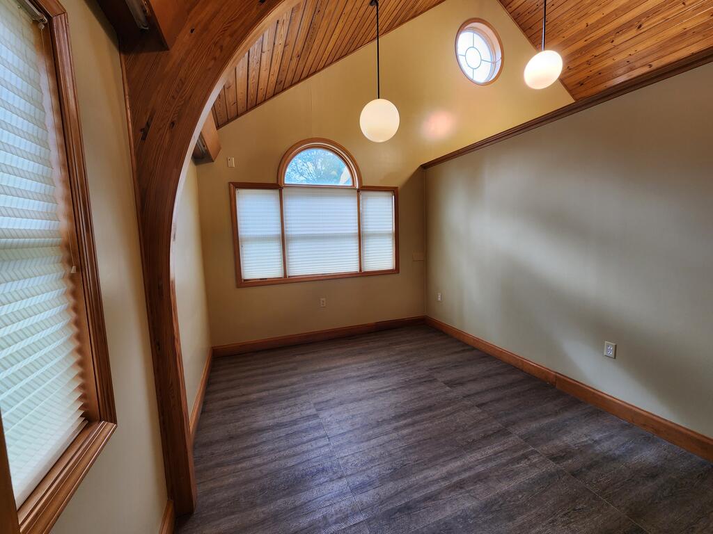 Empty room with a vaulted wood ceiling, arched doorway, and large windows.