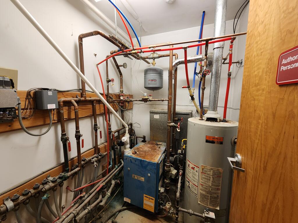 Utility room with a large water heater, boiler, and exposed plumbing.