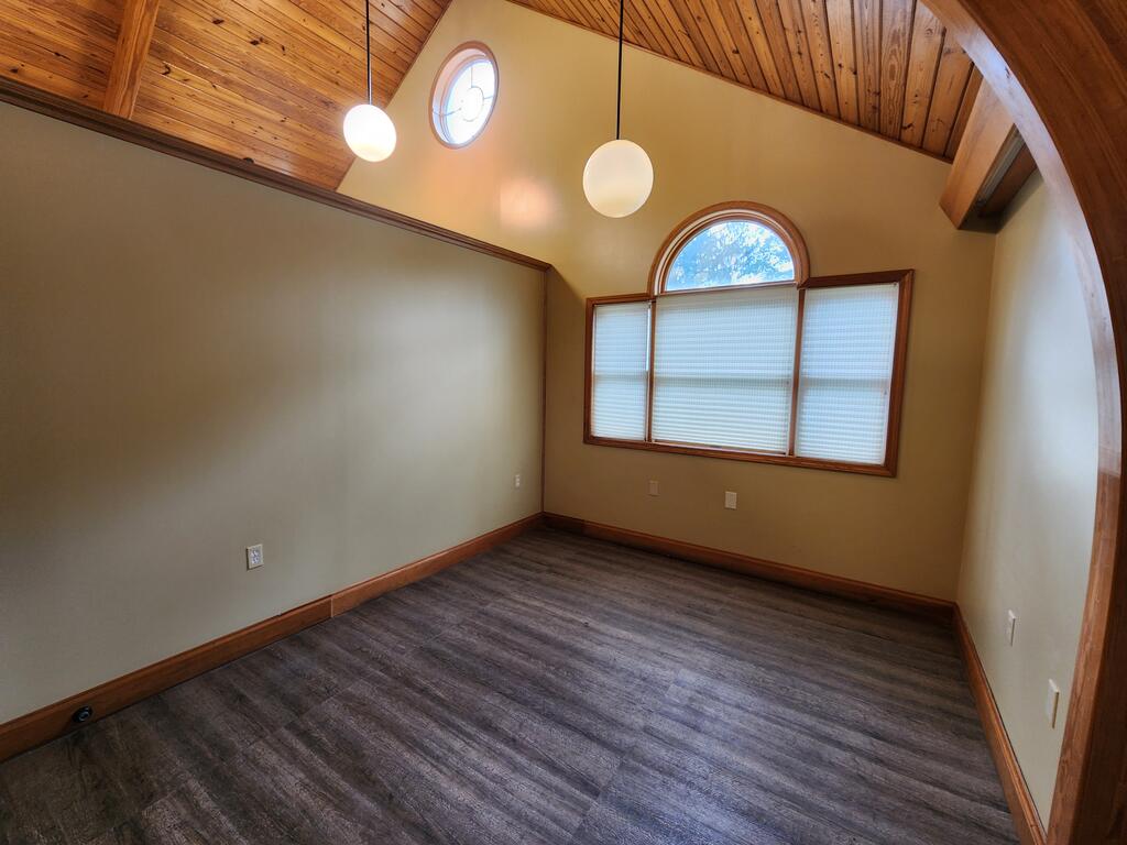Vacant room with a vaulted wood ceiling, arched windows, and dark flooring.