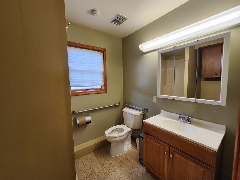 Bathroom with a wood vanity, mirrored cabinet, toilet, and grab bars.