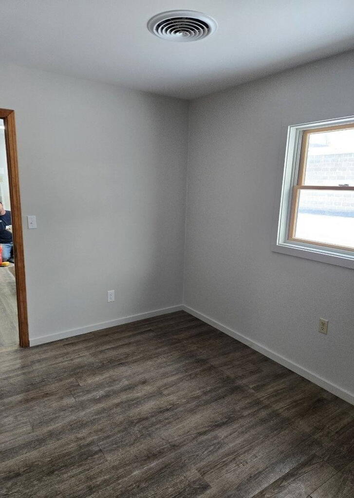Empty room with gray walls, dark plank flooring, and a window.