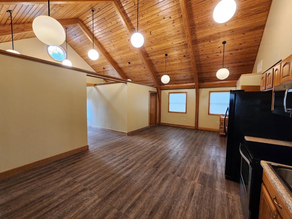 Open kitchen and dining area with a vaulted wood ceiling and dark plank flooring.