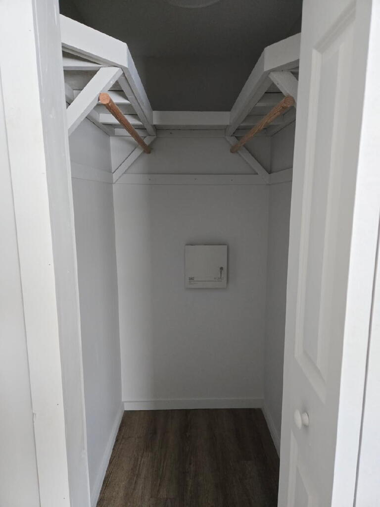 Walk-in closet with white shelving, wooden hanging rods, and dark wood-look flooring.