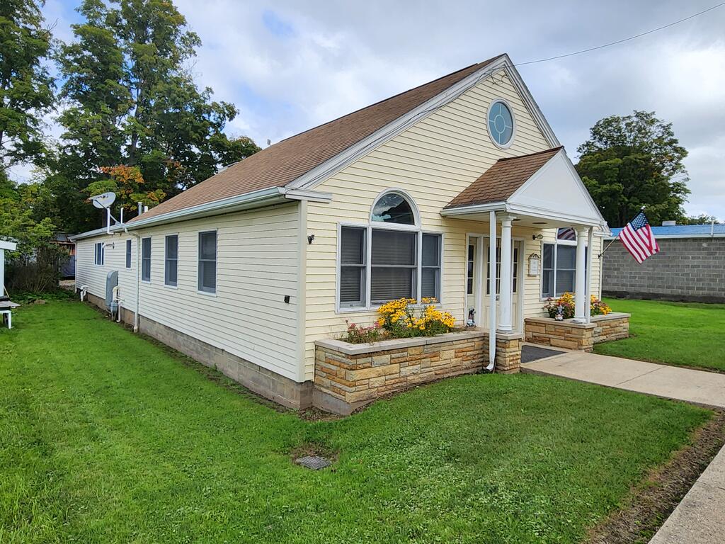 Cream-sided house with a steep gable roof, stone planter beds, and a covered entrance.