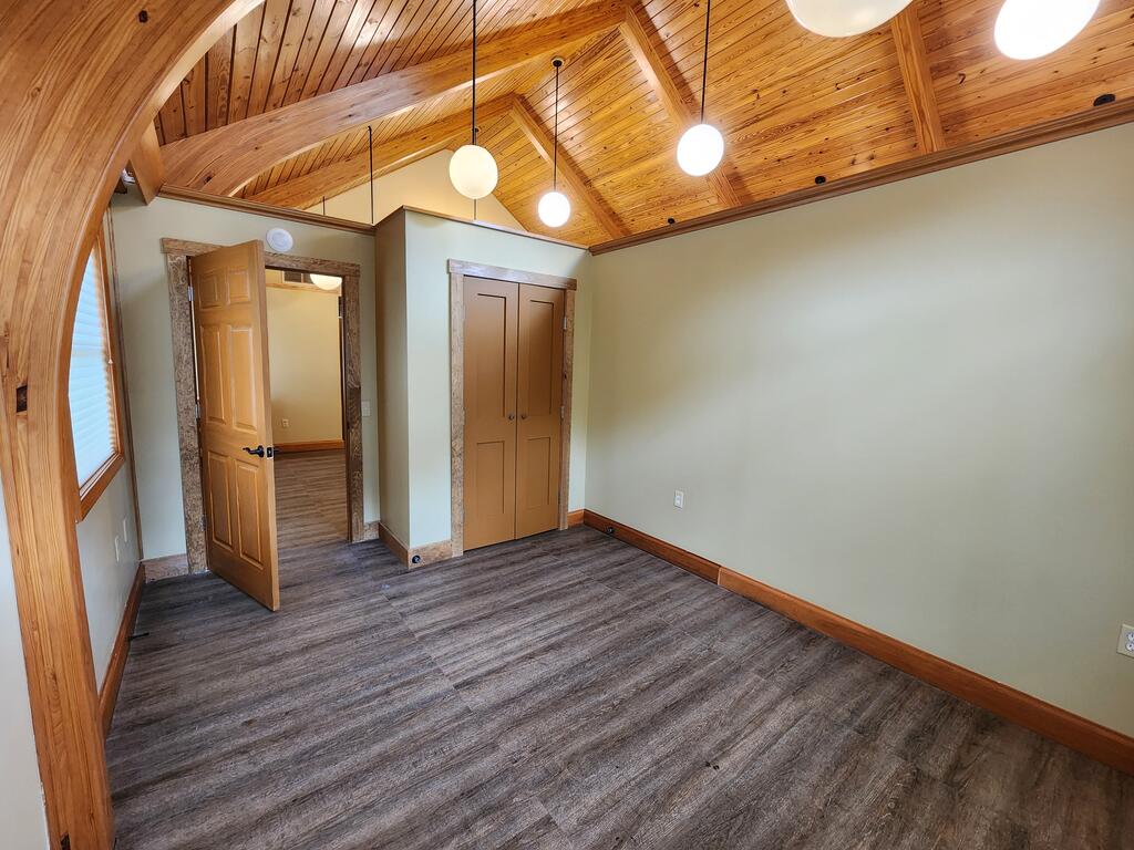 Empty room with a vaulted wood ceiling, exposed beams, and an arched window.