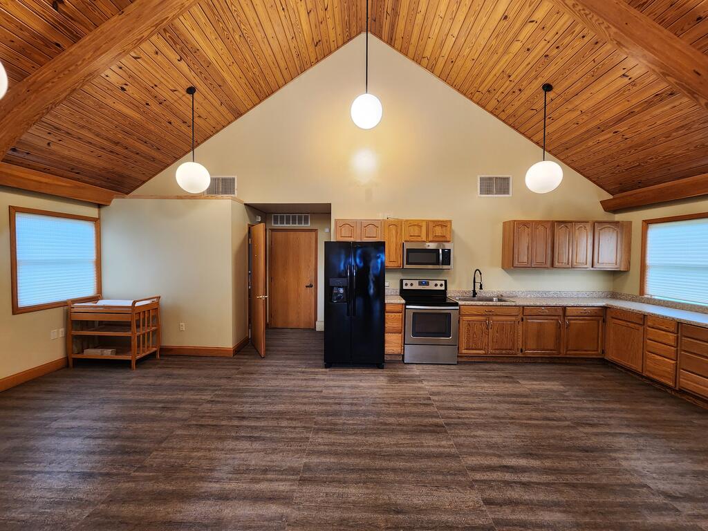 Kitchen with wood cabinetry and black appliances beneath a vaulted wood-plank ceiling.