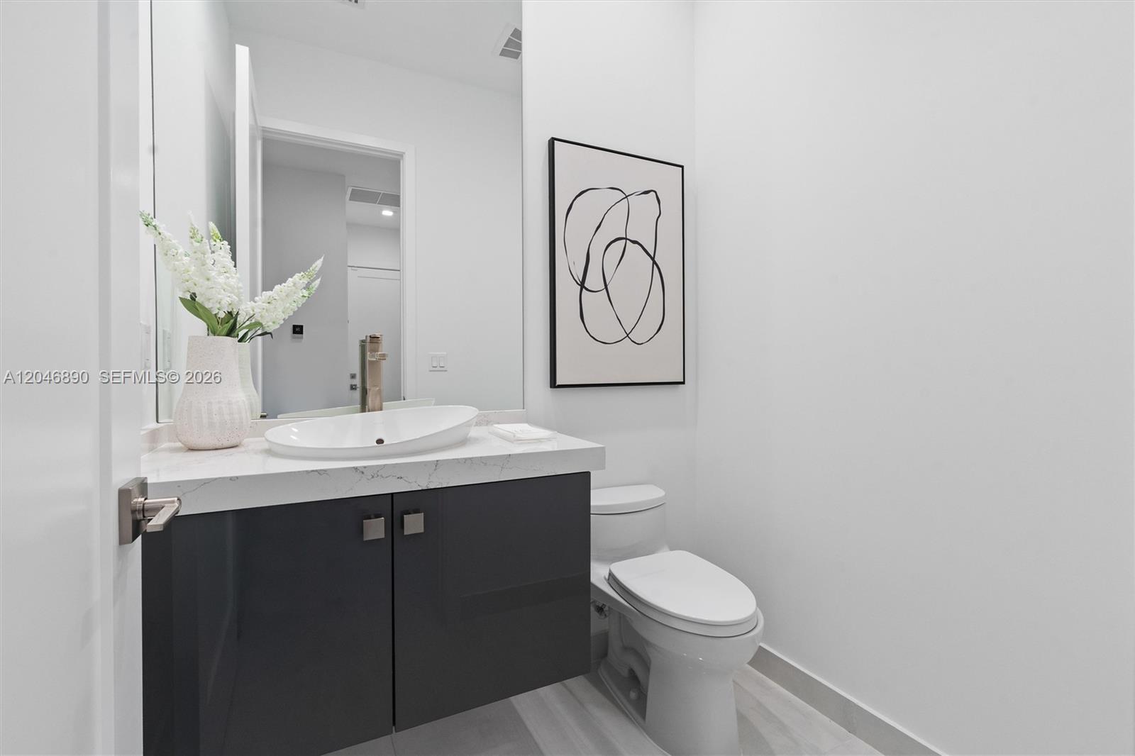 Modern bathroom with a dark floating vanity, white countertop, vessel sink, and toilet.