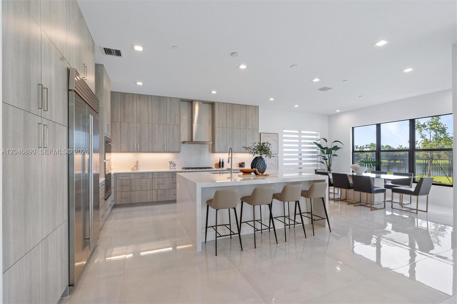 Modern kitchen with a large island, gray cabinetry, and dining area beside windows overlooking water.