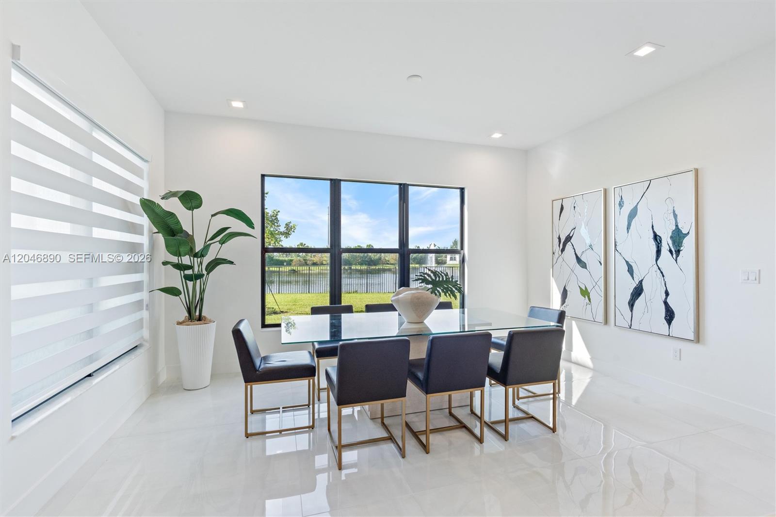 Dining room with a glass table, dark chairs, and large windows overlooking a lake.