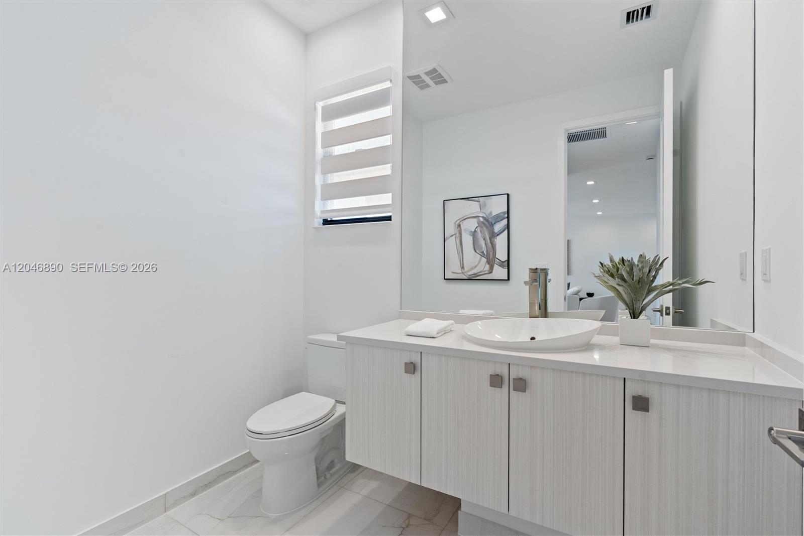 Modern bathroom with a floating white vanity, vessel sink, large mirror, and marble-look floor.