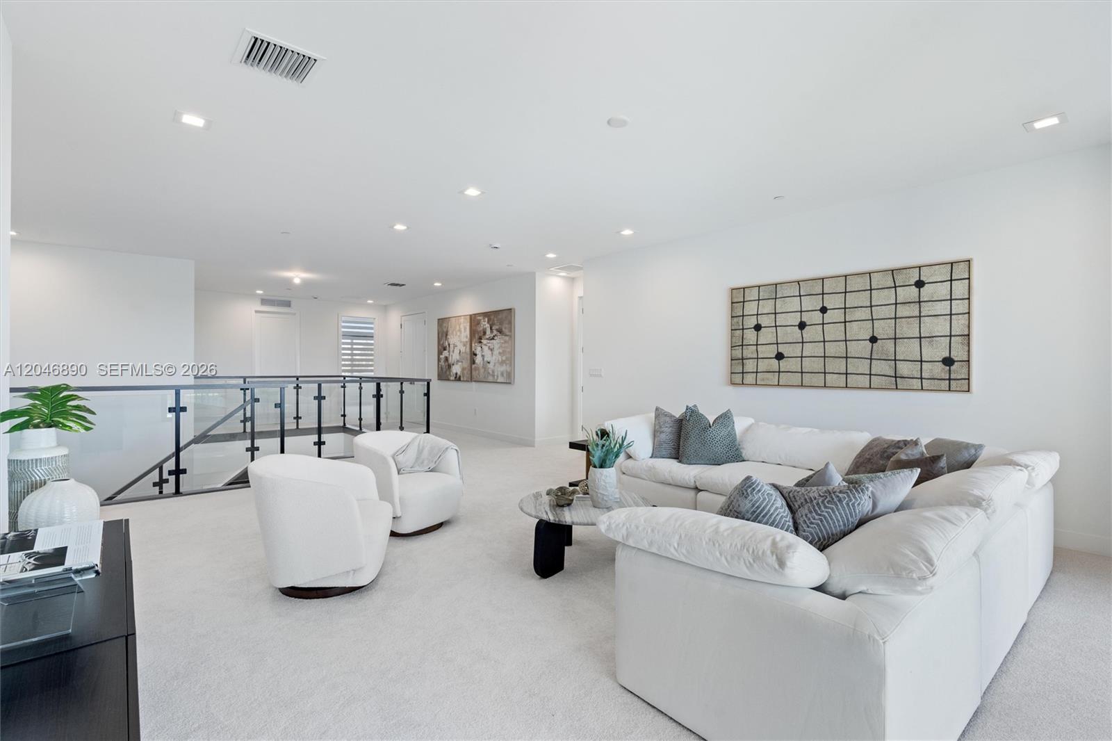 Upstairs living room with a white sectional, rounded accent chairs, and a glass stair railing.