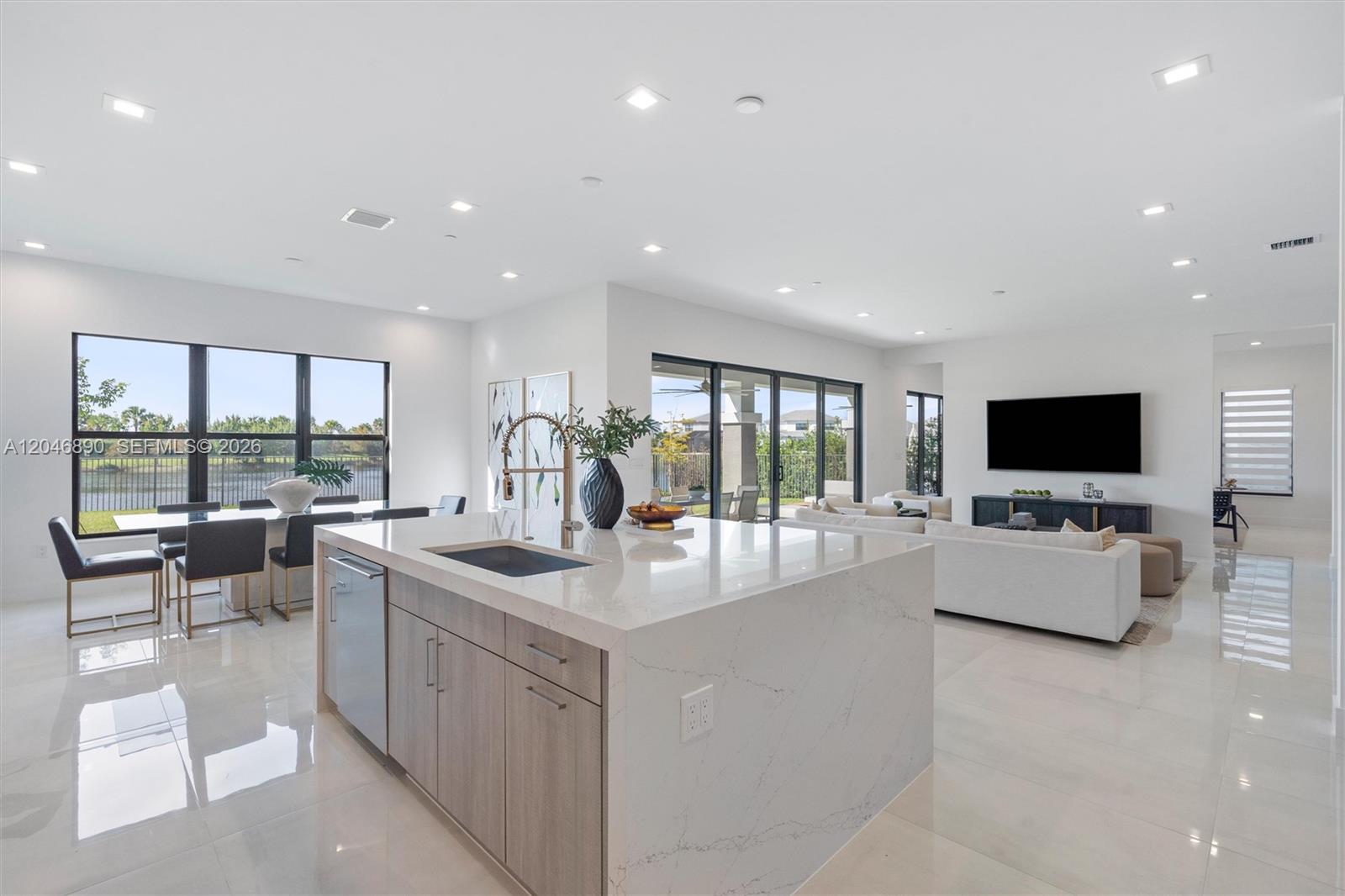 Open-plan kitchen with a large stone island, dining area, and living room overlooking water.