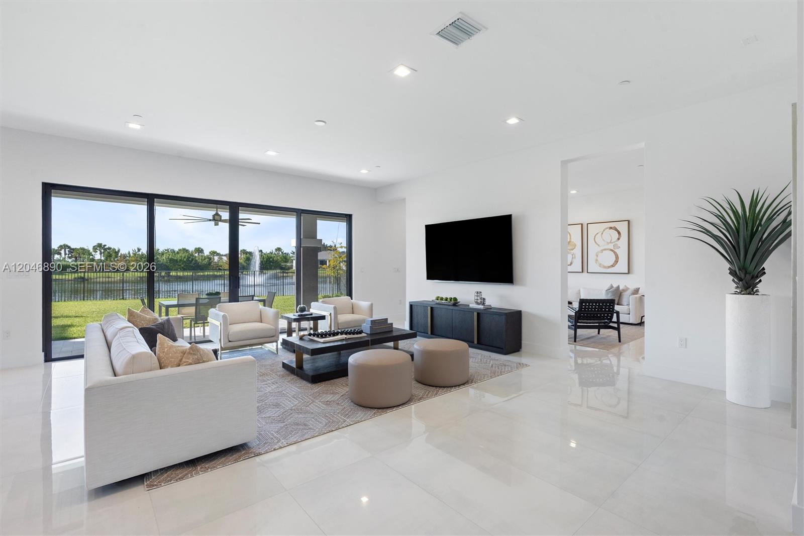 Living room with white seating and sliding glass doors overlooking a lake and fountain.