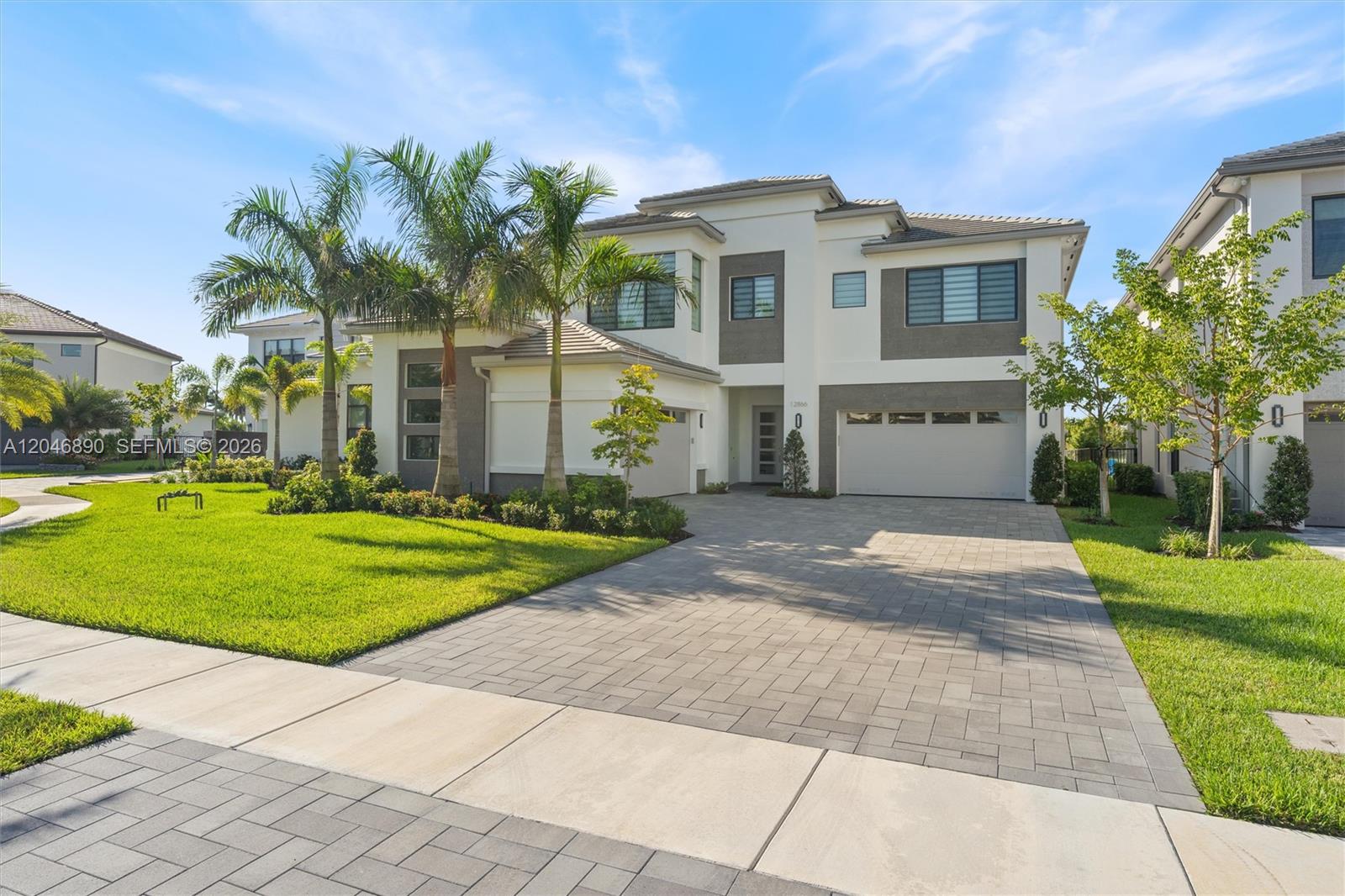 Modern two-story home with palm trees, landscaped lawn, and a wide paver driveway.