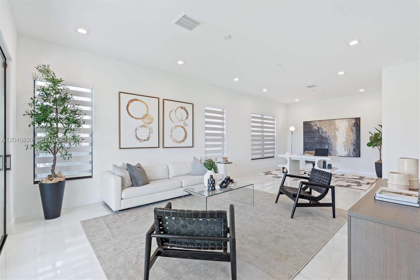 Staged living room with a white sofa, glass coffee table, and a desk in the background.