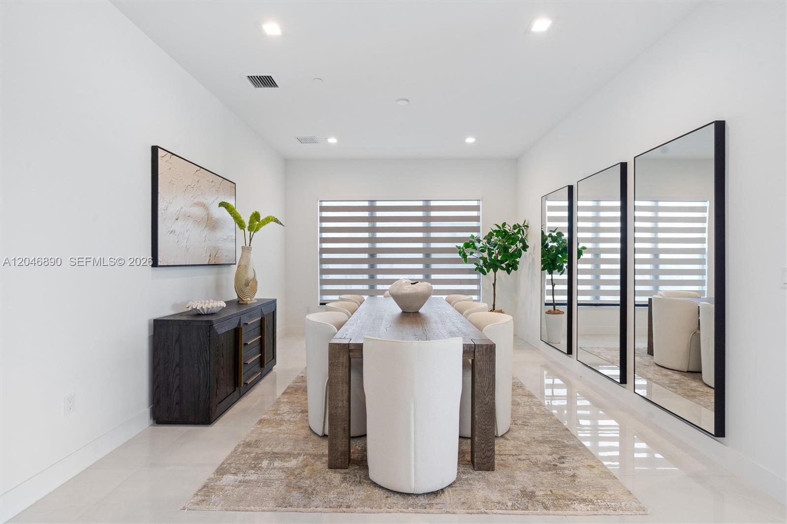 Staged dining room with a long wood table, white chairs, and full-length mirrors.