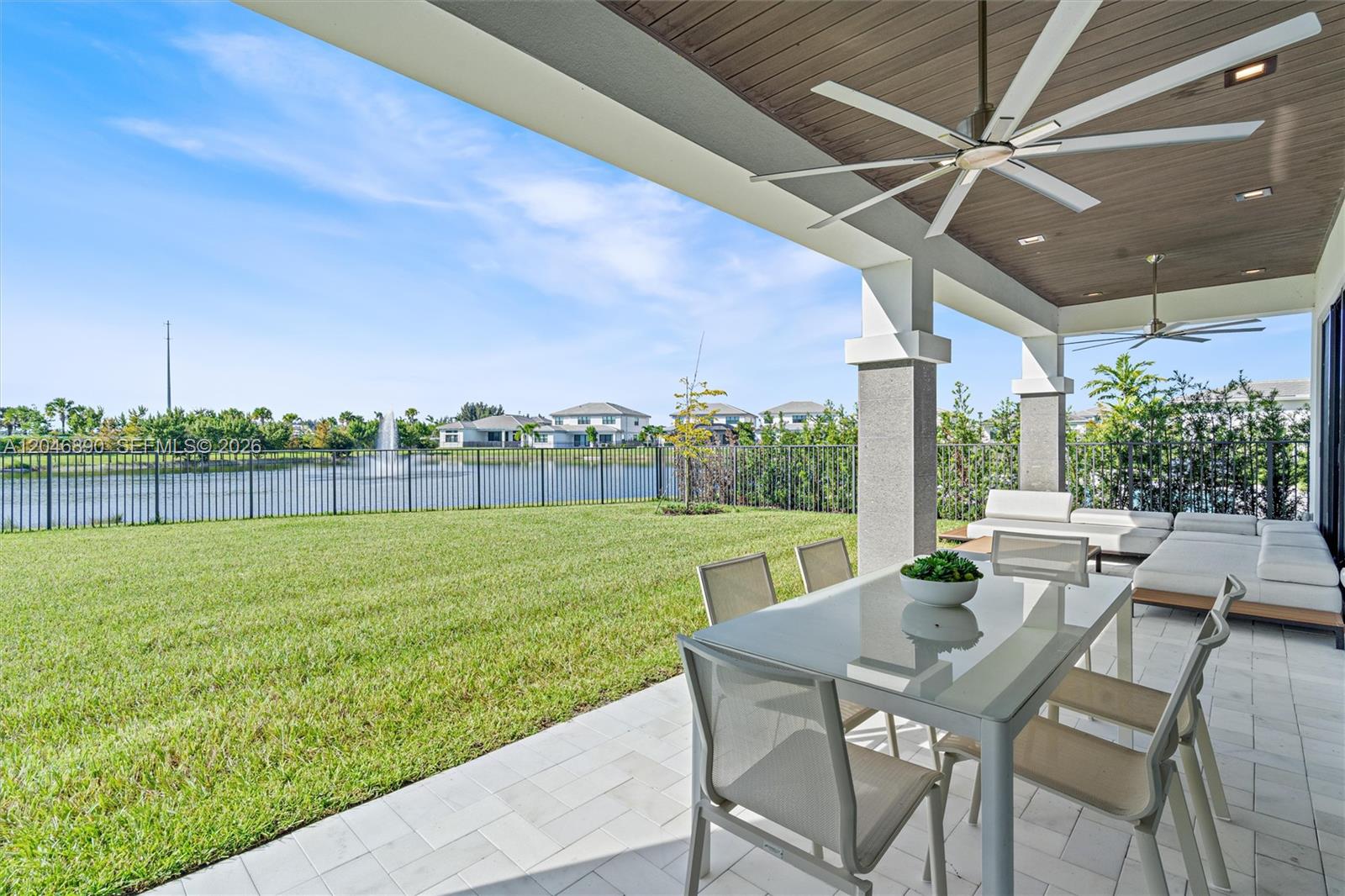 Covered patio with outdoor dining and lounge seating overlooking a lake and grassy lawn.