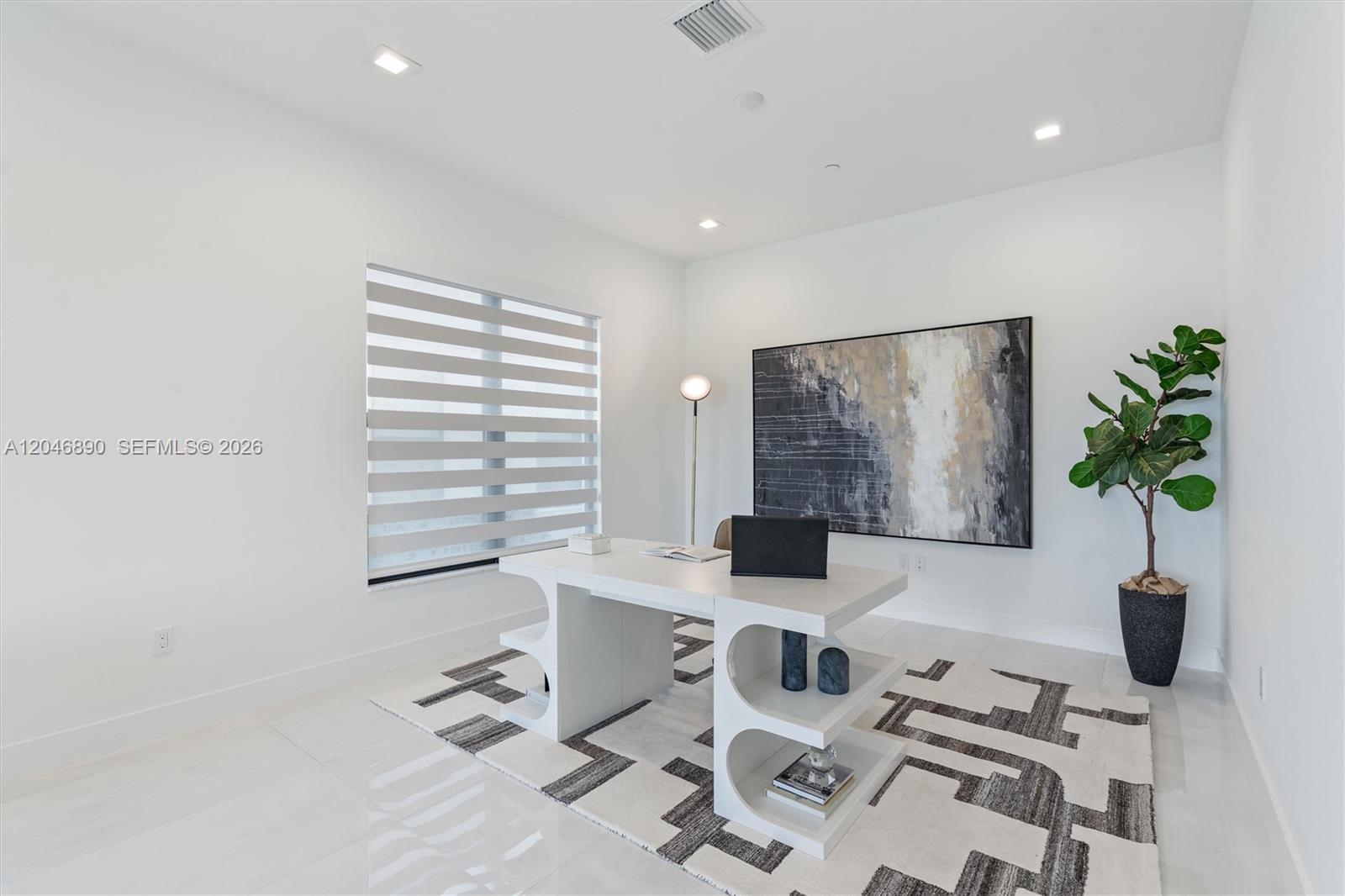 Modern white home office with a sculptural desk, geometric rug, abstract art, and potted tree.